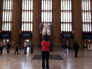 A person in red takes a photo of COMPANION art installation by KAWS at 30th Street Station